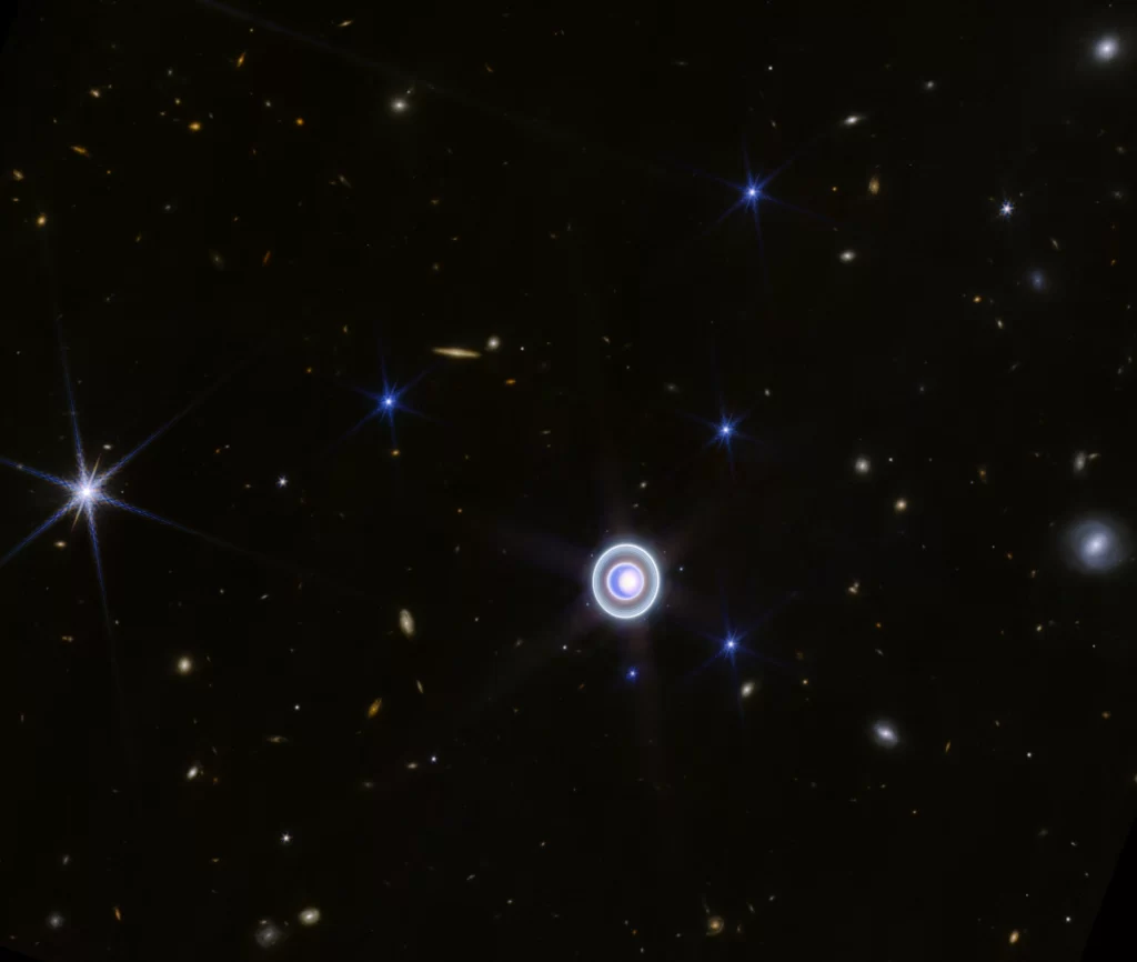 Ova širokokutna slika Urana snimljena NIRCam-om (Near-Infrared Camera) na NASA-inom svemirskom teleskopu James Webb prikazuje planet usred razasutih udaljenih galaksija u pozadini. Na ovoj slici prikazano je i 14 od ukupno 27 mjeseca planeta. NASA.