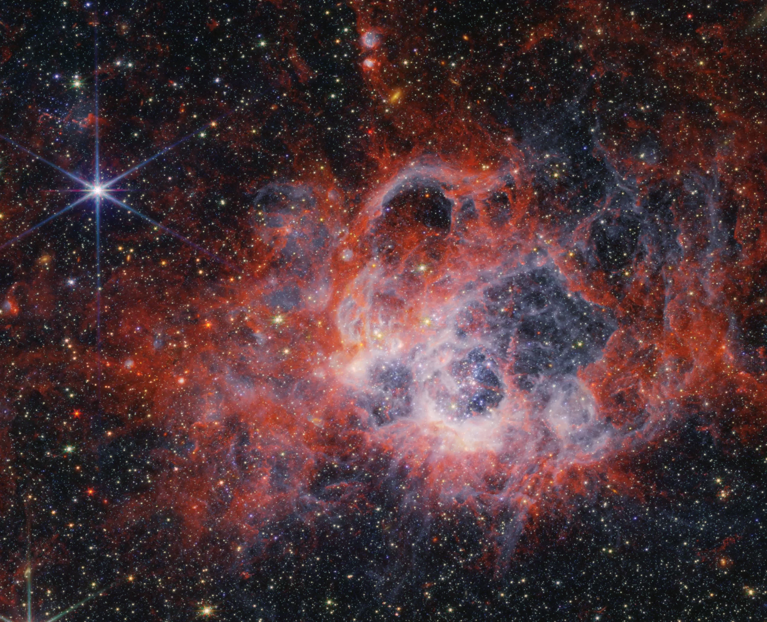 Ova slika regije formiranja zvijezda NGC 604, snimljena Near-Infrared kamerom (NIRCam) Svemirskog teleskopa James Webb NASA-e, prikazuje kako zvjezdani vjetrovi od sjajnih, vrućih, mladih zvijezda isklesavaju šupljine u okolnom plinu i prašini. NASA, ESA, CSA, STScI.