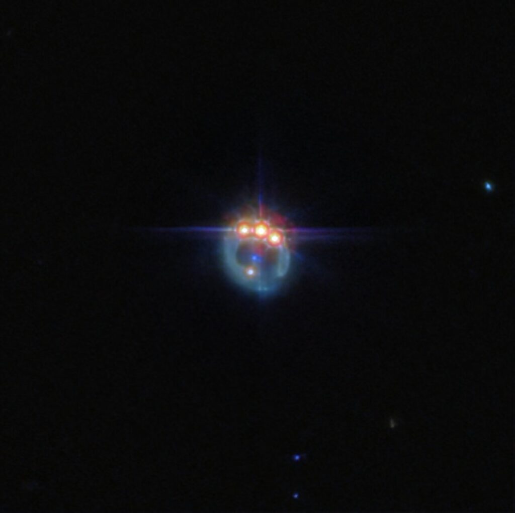 Fotografija galaksije iskrivljene gravitacijskom lećom u prigušeni prsten. Na vrhu prstena nalaze se tri vrlo svijetle točke s difrakcijskim šiljcima koji se protežu iz njih, smještene jedna pored druge: ovo su kopije jednog kvazara u lećastoj galaksiji, duplicirane gravitacijskom lećom. U središtu prstena, eliptična galaksija koja vrši lećenje pojavljuje se kao mala plava točka. Pozadina je crna i prazna. Kredit: ESA/Webb, NASA & CSA, A. Nierenberg.