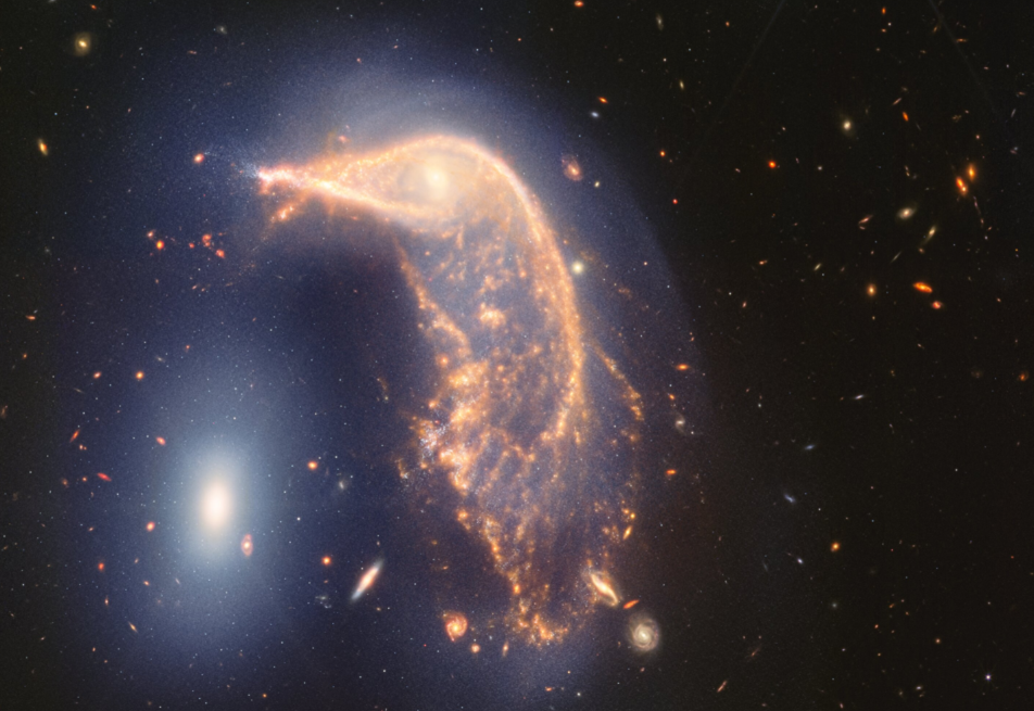 Iskrivljena spiralna galaksija u središtu, koja izgleda kao Pingvin, i kompaktna eliptična galaksija lijevo, koja izgleda kao Jaje, nalaze se u aktivnom 'zagrljaju'. Nova slika u bliskoj i srednjoj infracrvenoj svjetlosti, snimljena teleskopom James Webb povodom druge godine znanstvenih promatranja, pokazuje da je njihova interakcija obilježena blagim plavim sjajem u obliku obrnute slova U. Zasluge: NASA, ESA, CSA, STScI.