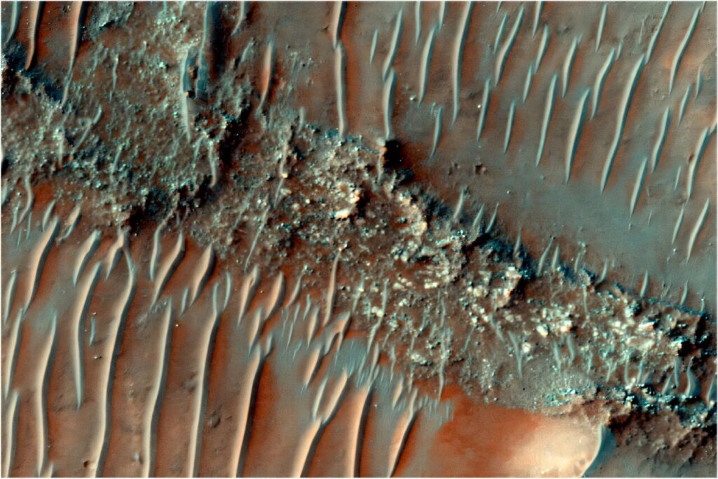 Obojena snimka ravnog, snažno erodiranog grebena FSR. Preko njegove površine prelaze pomične pješčane dine. Izvor: HiRISE snimka ESP_085386_1505, NASA/JPL/University of Arizona.