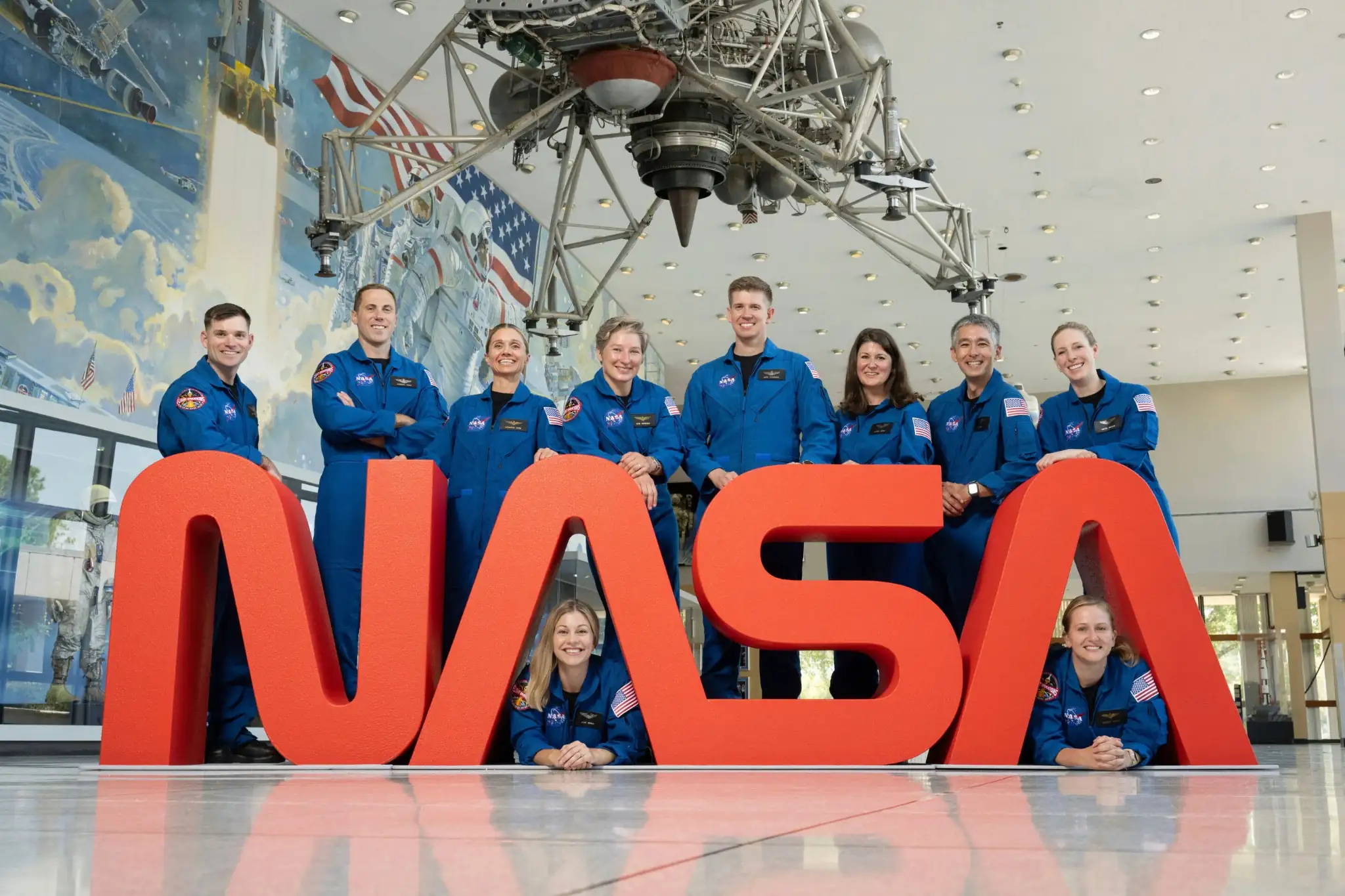 Na fotografiji koju je objavila NASA deset najnovijih astronauta pozira iza logotipa u Svemirskom centru Johnson u Houstonu, Teksas, 22. rujna 2025. Na slici su: stožerni narednik kopnene vojske SAD-a Ben Bailey, bojnik ratnog zrakoplovstva Cameron Jones, Katherine Spies, Anna Menon, poručnica bojnog broda mornarice SAD-a Erin Overcash, bojnik Adam Fuhrmann, Lauren Edgar, Yuri Kubo, Rebecca Lawler i dr. Imelda Muller. Izvor: NASA