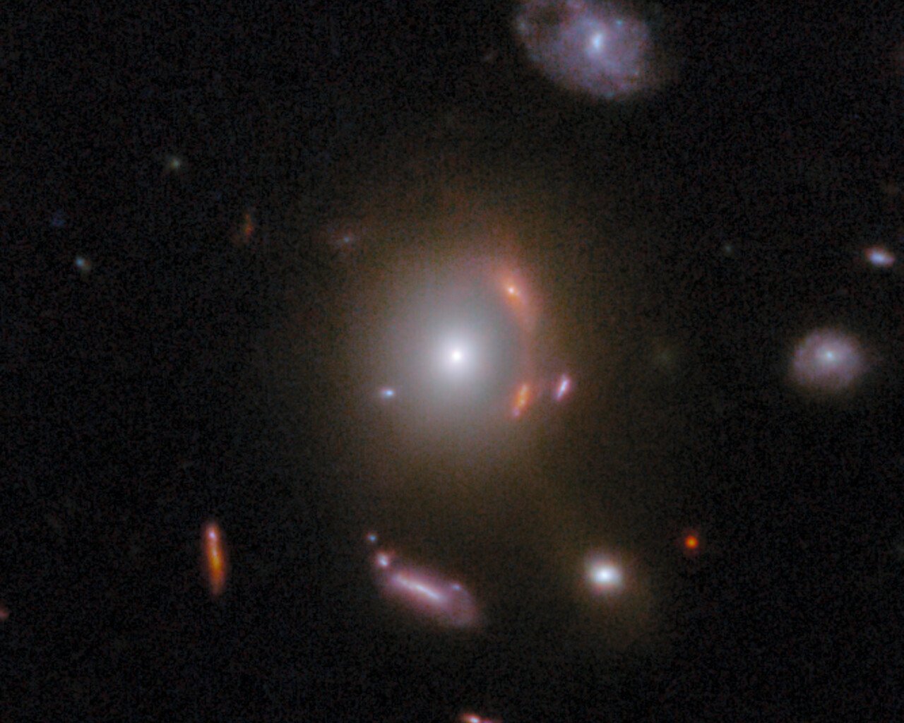 U prvom planu nalazi se središnja sjajna galaksija, dok se uz njezinu desnu stranu pruža narančasti luk – izobličena pozadinska galaksija čiju je svjetlost savila gravitacija. Zasluge: ESA/Webb, NASA i CSA, G. Gozaliasl, A. Koekemoer, M. Franco