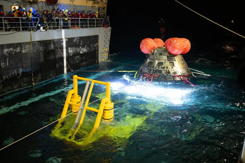 Ronioci američke ratne mornarice i astronauti misije Artemis II na napuhujućem čamcu prilaze helikopterima koji ih potom prebacuju na brod za prihvat nakon izlaska iz NASA-ine letjelice Orion. Orion je prevozio zapovjednika misije Artemis II Reida Wisemana, pilota Victora Glovera i specijalisticu misije Christinu Koch iz NASA-e, kao i specijalista misije Jeremyja Hansena iz Kanadske svemirske agencije, nakon spuštanja u Tihi ocean u blizini San Diega u Kaliforniji u 17:07 po pacifičkom vremenu, odnosno 20:07 po istočnoameričkom vremenu, u petak 10. travnja 2026. Probni let Artemis II poletio je u srijedu 1. travnja iz NASA-ina Svemirskog centra Kennedy na Floridi i time započeo desetodnevno putovanje oko Mjeseca, s ciljem znanstvenih istraživanja, gospodarskih koristi i nadogradnje temelja za prve misije s ljudskom posadom prema Marsu. NASA-in tim za prihvat i oporavak te pripadnici američke vojske pomažu posadi Artemis II pri izlasku iz letjelice Orion. Zasluge za fotografiju: NASA / James Blair
