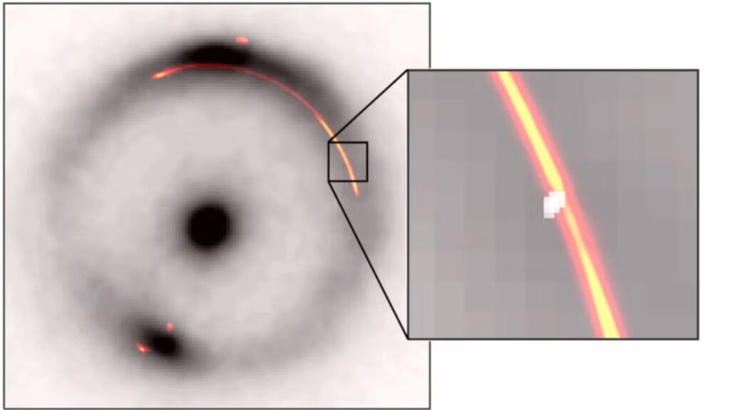 Sustav gravitacijske leće JVAS B1938+666. Crni prsten i središnja točka prikazuju infracrvenu snimku udaljene galaksije izobličene gravitacijskim lećenjem. Narančasto zračenje prikazuje radiosignal iz istog sustava. U uvećanom prikazu vidi se malo suženje na slici koje uzrokuje dodatni kompaktni objekt mase oko milijun puta veće od mase Sunca, prikazan kao bijela mrlja. Zasluge: Devon Powell, Institut Max Planck za astrofiziku, na temelju podataka Keck/EVN/GBT/VLBA.