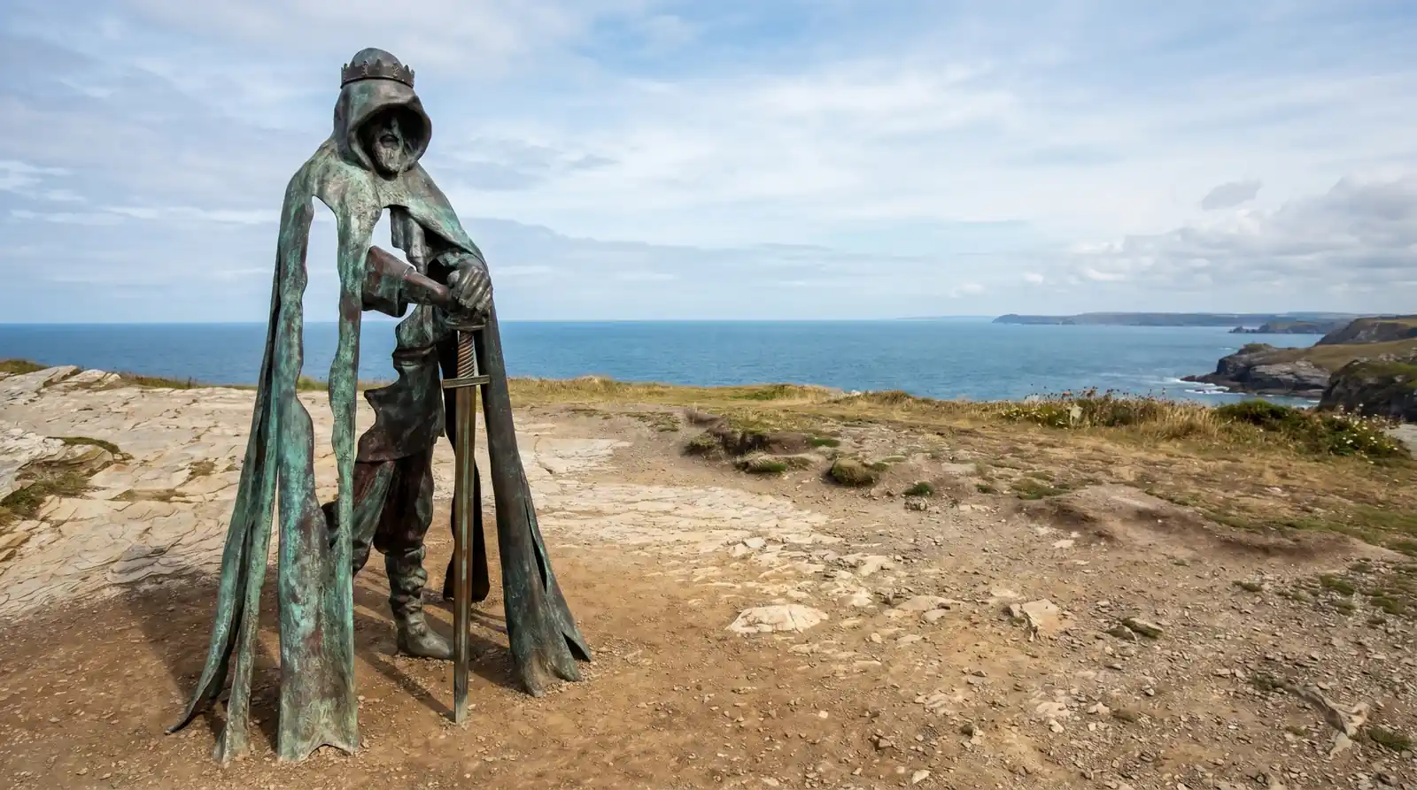 Brončani kip kralja Artura s mačem, smješten na litici iznad mora.