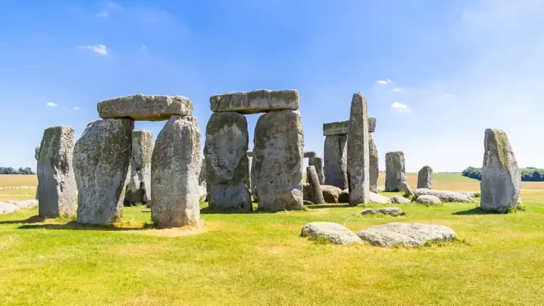 Stonehenge na otvorenom krajoliku pod vedrim plavim nebom, s velikim kamenim blokovima i travnatom površinom u prvom planu.