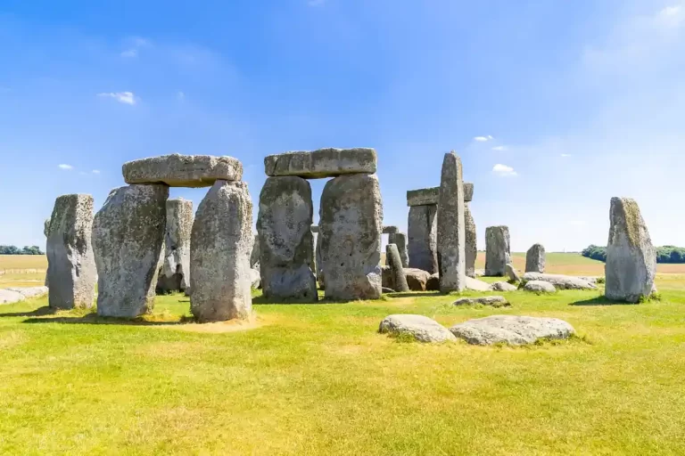 Stonehenge na otvorenom krajoliku pod vedrim plavim nebom, s velikim kamenim blokovima i travnatom površinom u prvom planu.