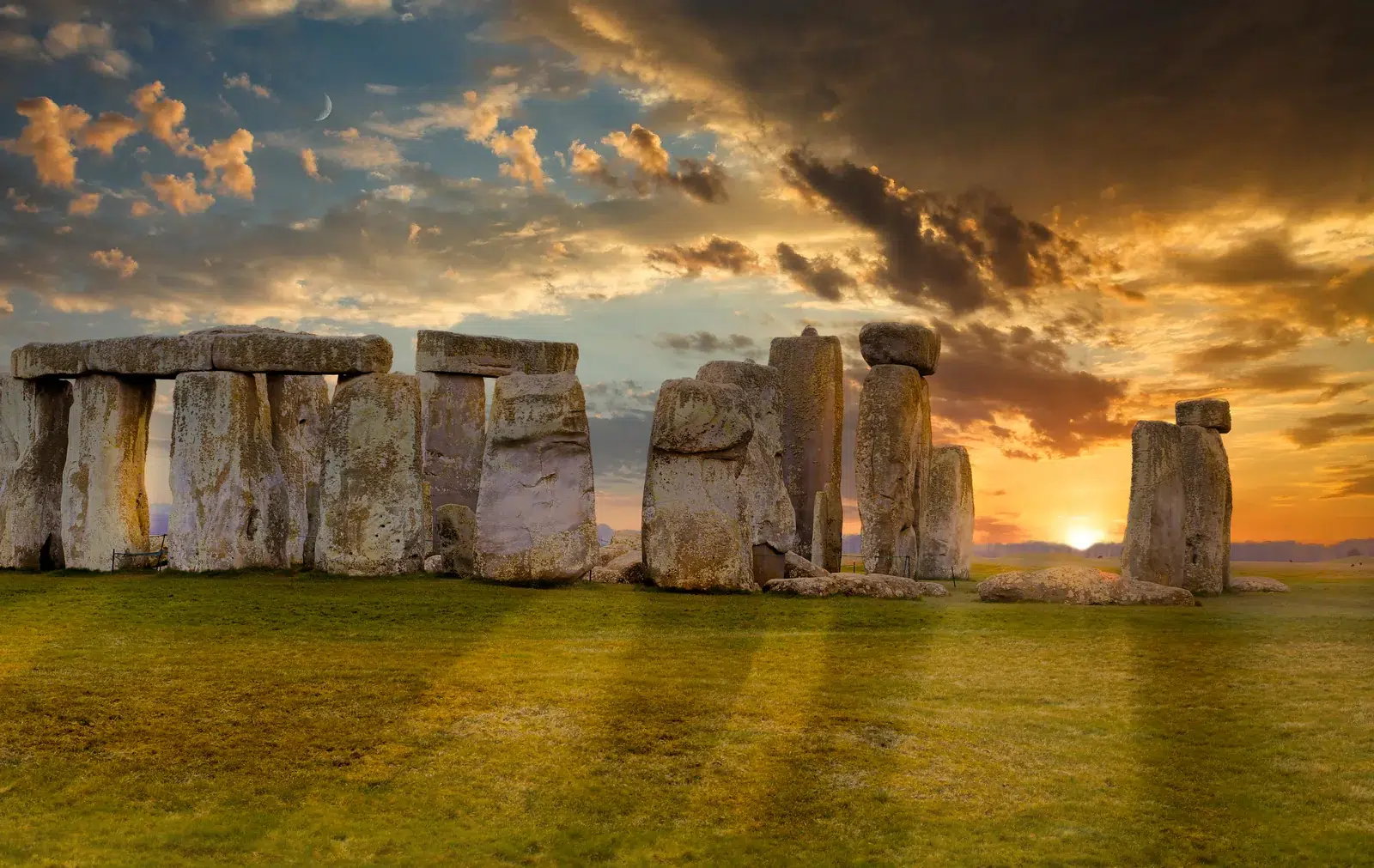 Stonehenge u Engleskoj pri zalasku Sunca, s velikim kamenim blokovima u prvom planu i dramatičnim nebom iznad horizonta.