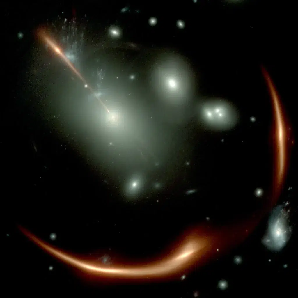 Fotografija Svemirskog teleskopa James Webb (JWST) prikazuje snažno izobličenu crvenu galaksiju MRG-M0138, viđenu kroz prednji skup galaksija, prikazan kao bijeli izvori svjetlosti. Zbog gravitacijske leće ista pozadinska galaksija vidi se četiri puta. Bijeli kvadrat označava najviše povećanu sliku, koju su Newman i suradnici proučavali instrumentom NIRSpec Integral Field Spectrograph na JWST-u. Zasluge: James Webb.