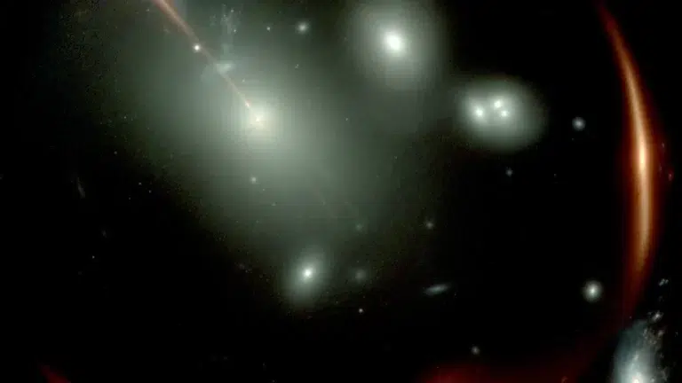 Fotografija Svemirskog teleskopa James Webb (JWST) prikazuje snažno izobličenu crvenu galaksiju MRG-M0138, viđenu kroz prednji skup galaksija, prikazan kao bijeli izvori svjetlosti. Zbog gravitacijske leće ista pozadinska galaksija vidi se četiri puta. Bijeli kvadrat označava najviše povećanu sliku, koju su Newman i suradnici proučavali instrumentom NIRSpec Integral Field Spectrograph na JWST-u. Zasluge: James Webb.