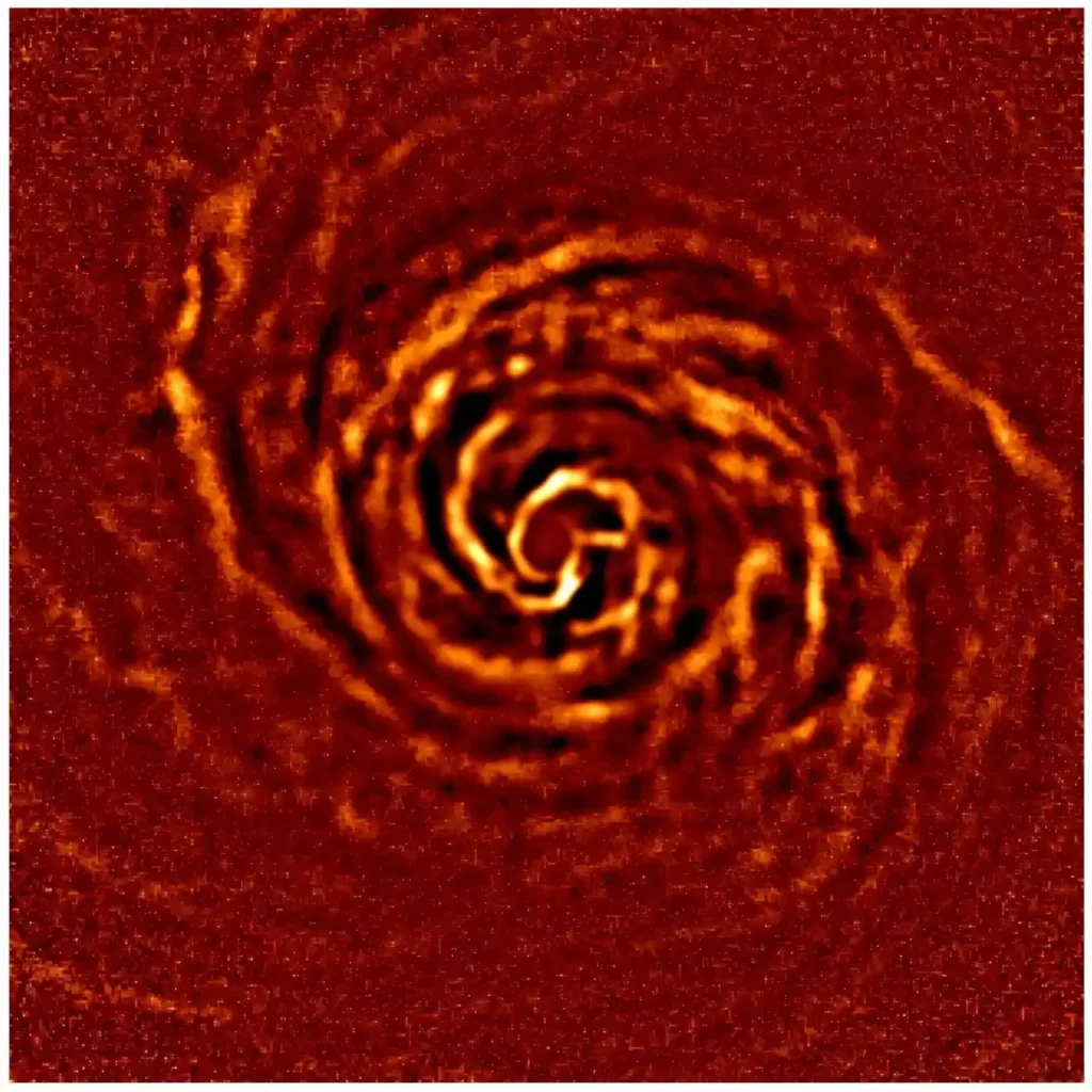 Protoplanetarni disk oko mlade zvijezde AB Aurigae prikazan u narančasto-crvenim tonovima, sa spiralnim strukturama prašine i plina oko središta diska.