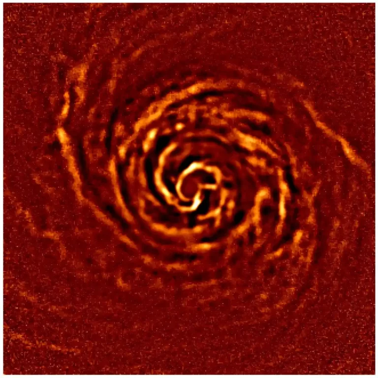 Protoplanetarni disk oko mlade zvijezde AB Aurigae prikazan u narančasto-crvenim tonovima, sa spiralnim strukturama prašine i plina oko središta diska.