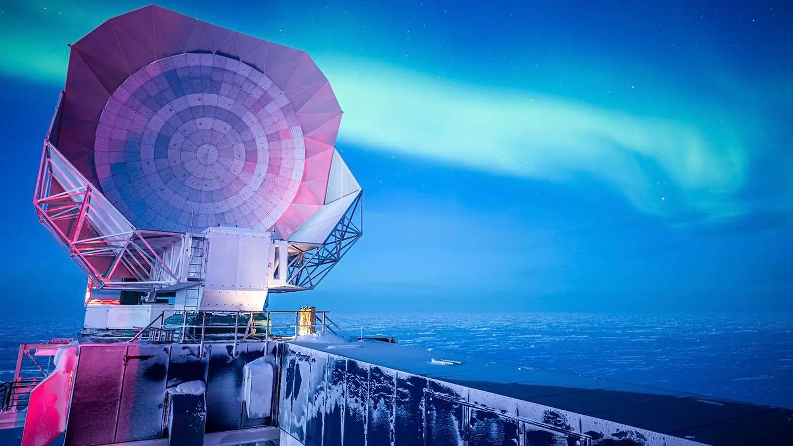 South Pole Telescope na Antarktici pod polarnom svjetlosti, s ledenim krajolikom i vedrim noćnim nebom u pozadini.