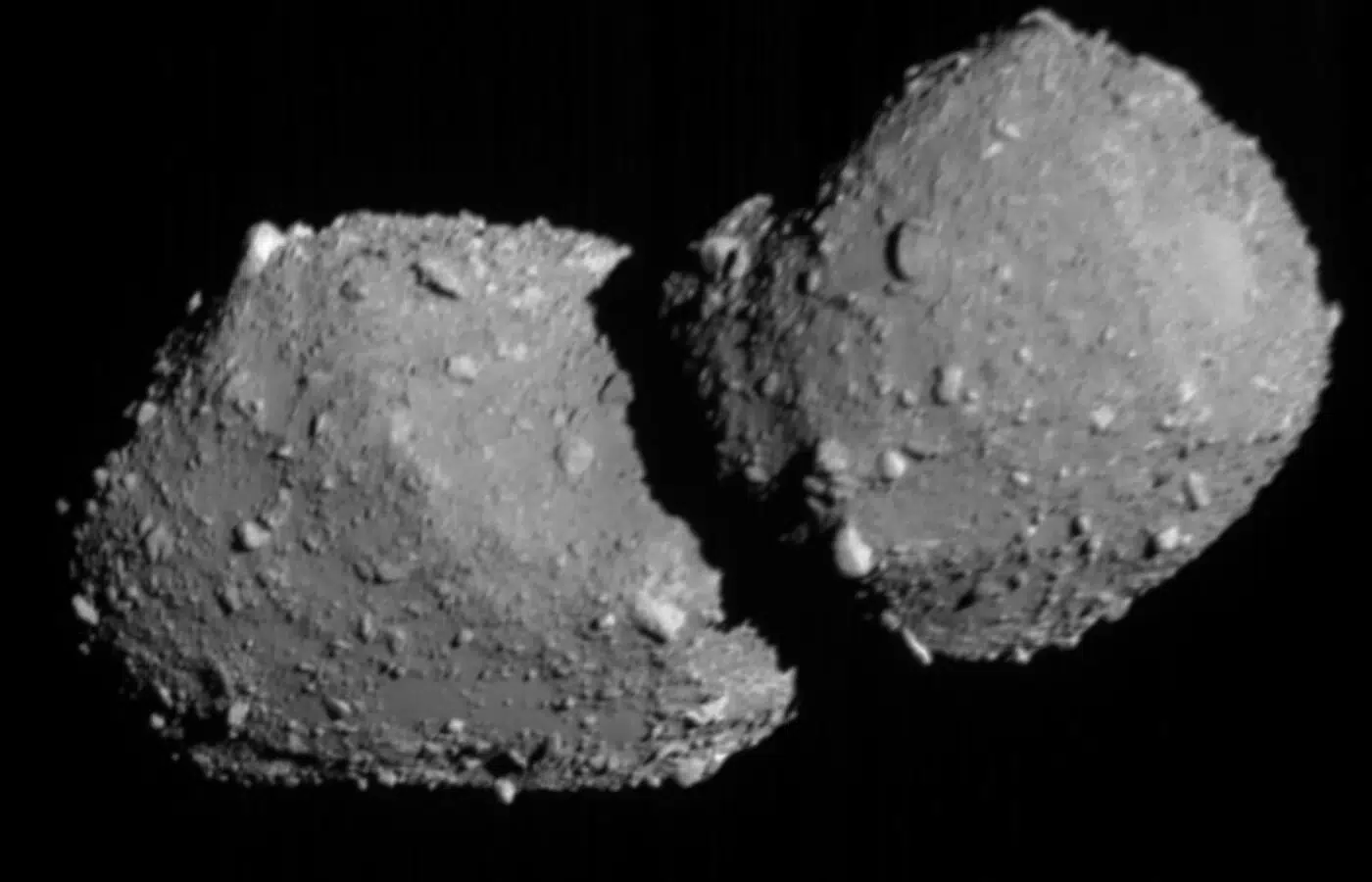 Crno-bijela snimka asteroida Torifune s dva spojena, nepravilno zaobljena dijela i kamenitom površinom na tamnoj pozadini svemira.