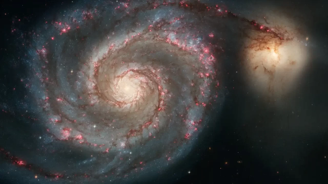 Spiralna galaksija M51 s plavim i ružičastim područjima nastanka zvijezda te manjom galaksijom uz njezin rub