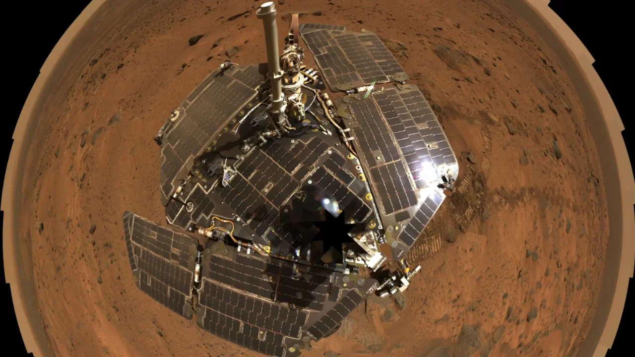Pogled odozgo na NASA-in rover Spirit s raširenim solarnim panelima na crvenkastom, kamenitom tlu Marsa.