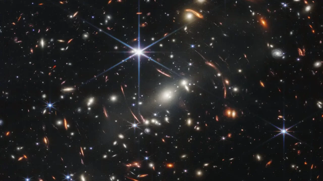 Infracrvena snimka prikazuje skup galaksija MACS J0308.9+2645 i mnoštvo udaljenih galaksija razasutih po tamnoj pozadini svemira. Zasluge: NASA/ESA/CSA/STScI