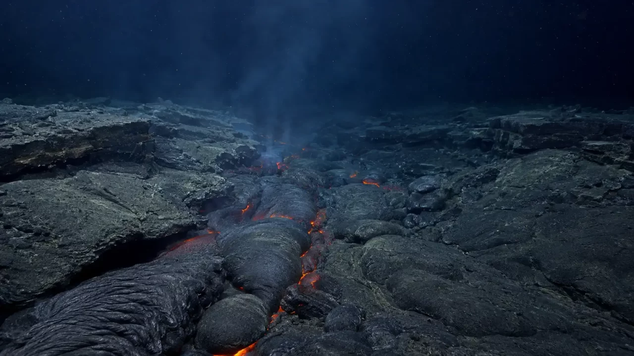 Podvodni pogled na pukotinu na dnu oceana iz koje istječe svježa lava, okružena tamnim bazaltnim stijenama i svijetlim mineralnim oblakom.