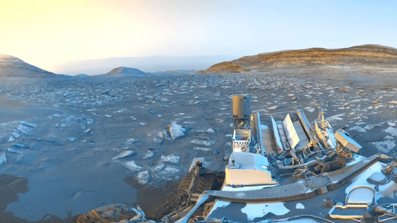 Curiosity i tragovi njegovih kotača u panorami kratera Gale, obrađenoj u plavim i žutim nijansama.
