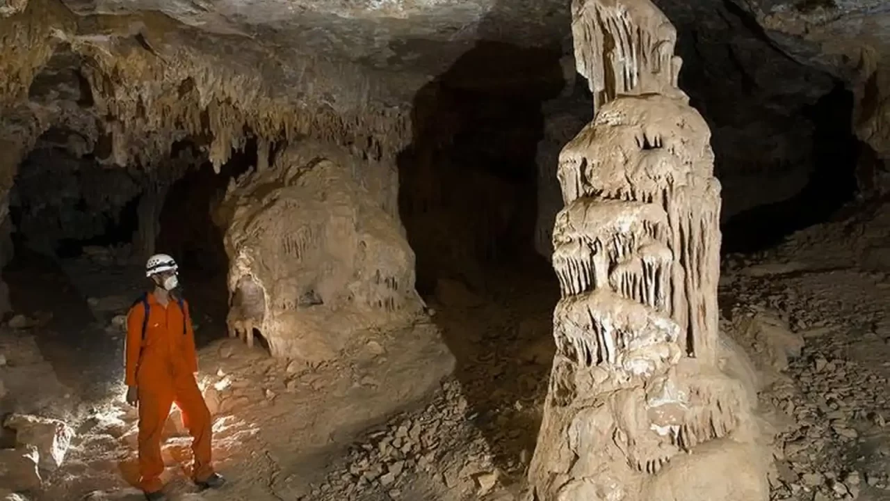 Istraživač u narančastom odijelu stoji uz velike stalagmite u špilji južno od Atlasa.