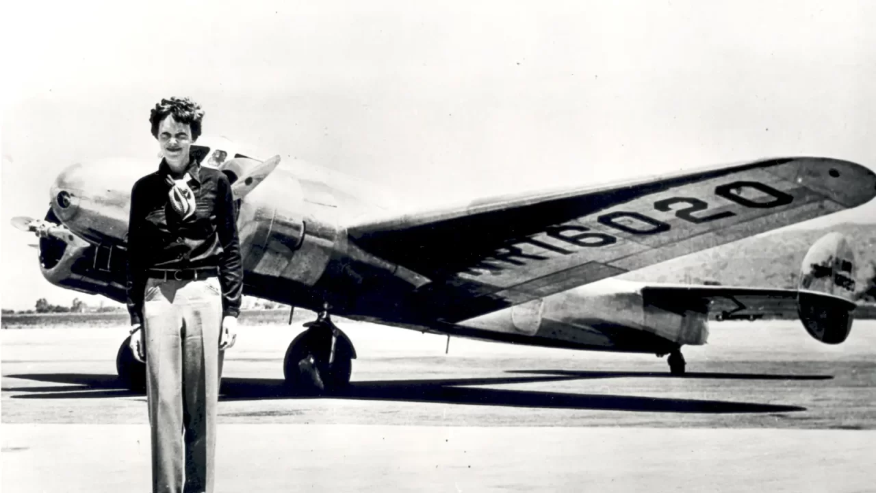 Amelia Earhart stoji ispred dvomotornog zrakoplova Lockheed Electra na crno-bijeloj arhivskoj fotografiji.