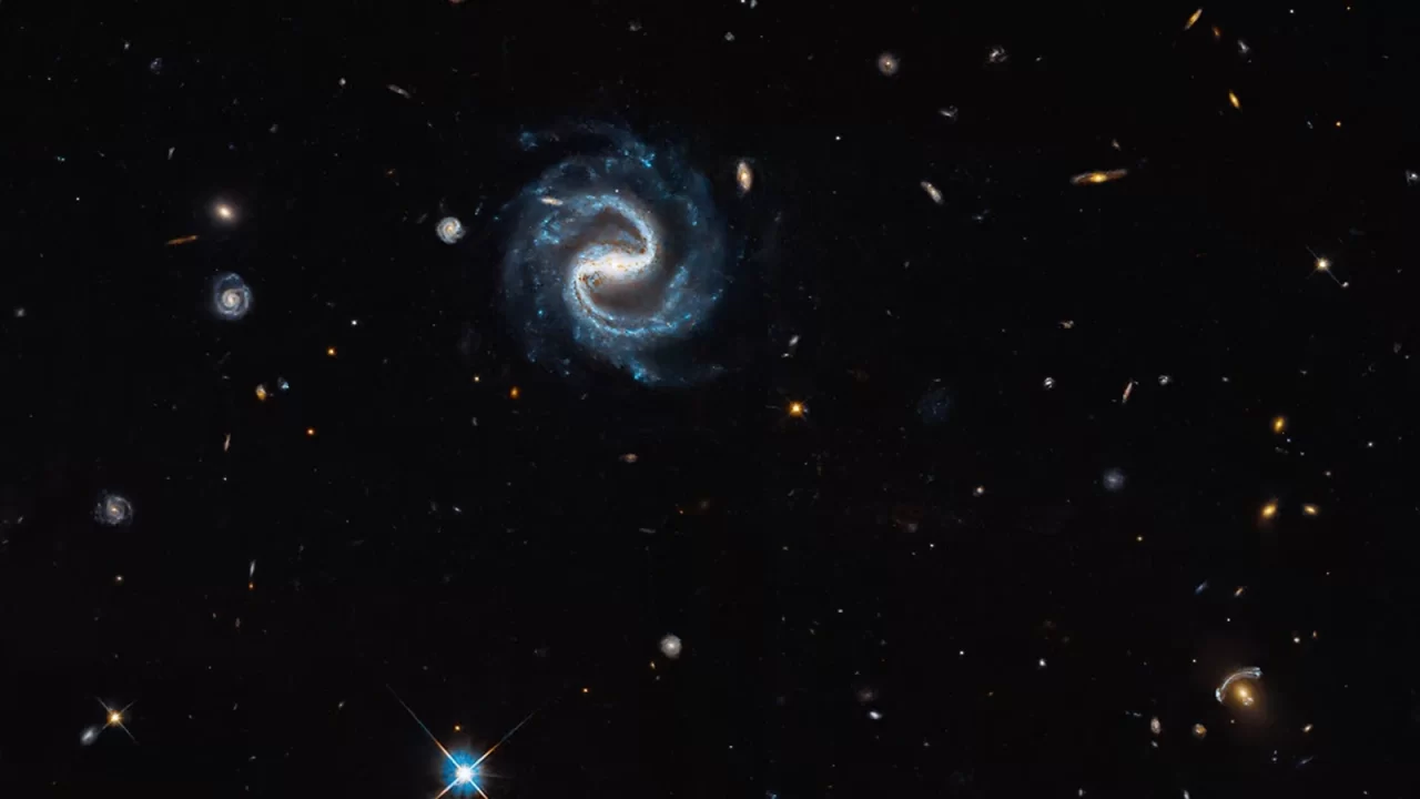 Spiralna galaksija i, desno ispod nje, žućkasta galaksija okružena plavičastim lukovima gravitacijske leće