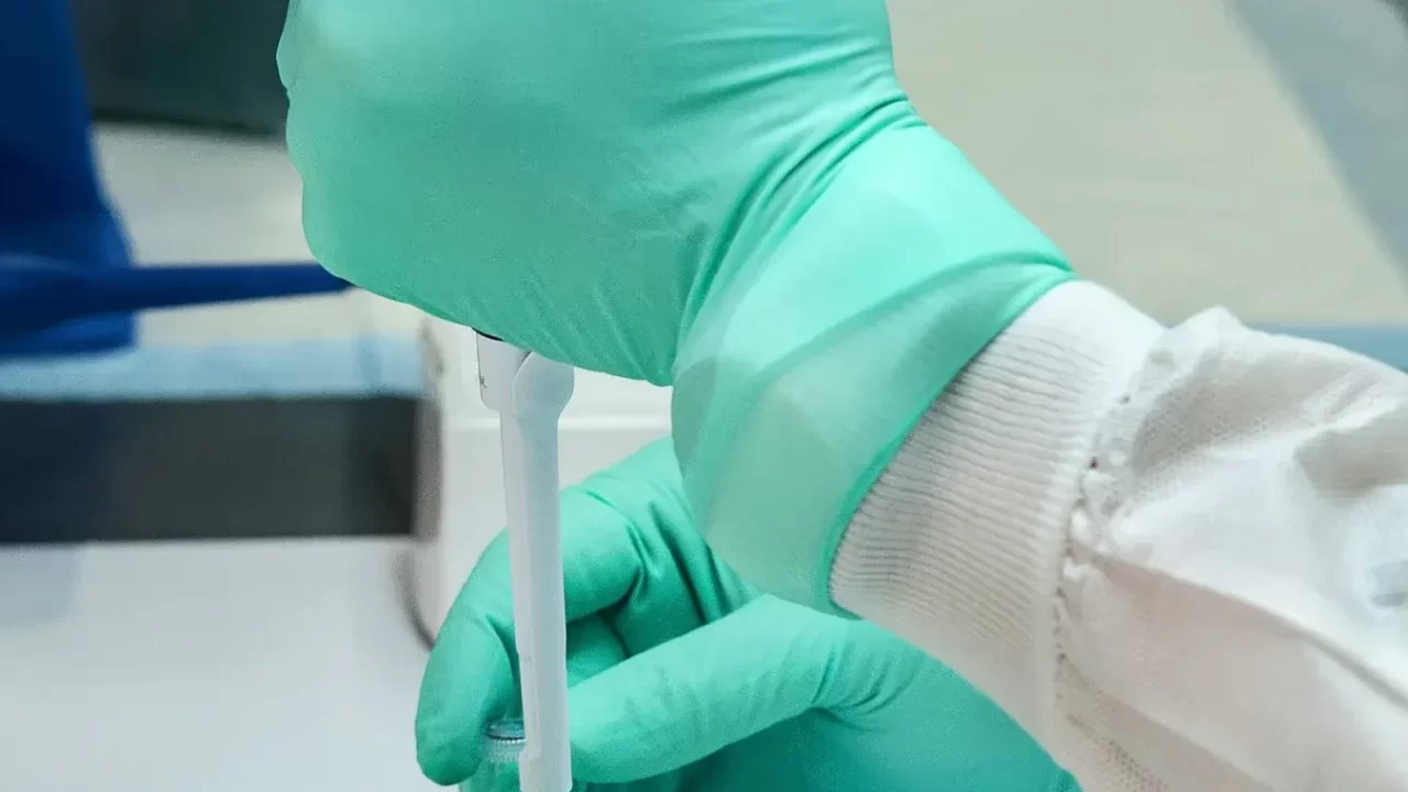 Ruke u zelenim zaštitnim rukavicama drže pipetu u laboratoriju.