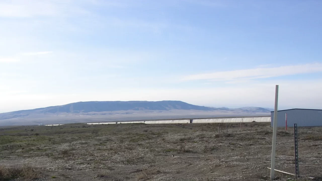 Dugi ravni krak detektora LIGO u suhom krajoliku Hanforda, s brežuljcima u pozadini.