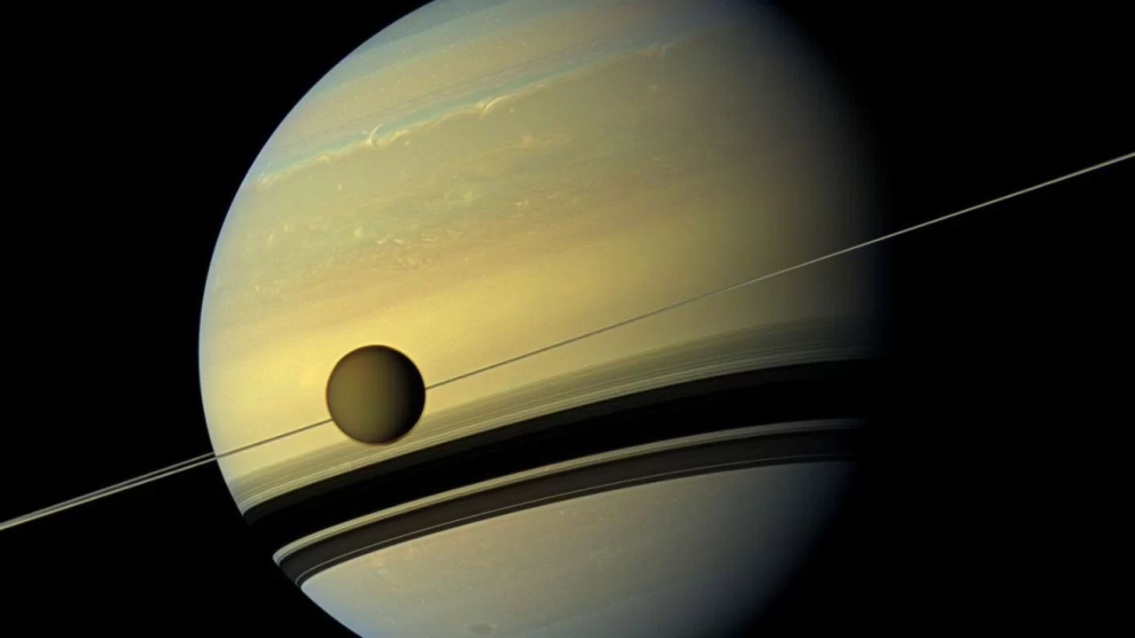Saturn s prstenovima i Titanom ispred planeta na Cassinijevoj snimci.